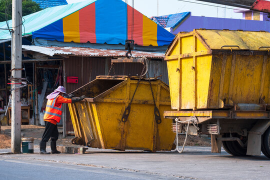 Asian Garbage Worker Is Moving Yellow Dumpster On Garbage Truck Into Community Dump Area 