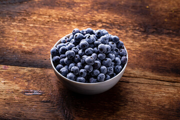 Fresh blueberries in a bowl on a brown wooden background.