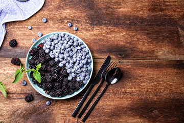 blueberries and blackberries on a plate on a dark wooden background with cutlery. The concept of vegetarianism, healthy food.
