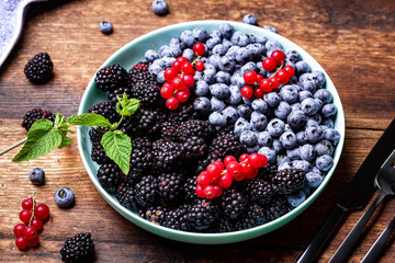 Different mixture of berries - blueberries, blackberries and red currants in a plate on a wooden background. Fruit, berry background.