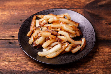 Fried potatoes on a black plate on a wooden background.