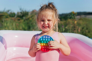 Little cute girl swims in the pool and plays with an anti-stress pop-it toy. Summer rest. Happy childhood