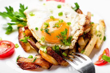 Fried potatoes with egg with liquid flowing yolk, herbs and tomatoes on a white plate.