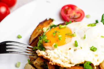 Fried potatoes with egg with liquid flowing yolk, herbs and tomatoes on a white plate.
