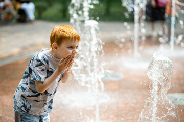 Young boy in the summer fountain in the park. Summer vacation time.