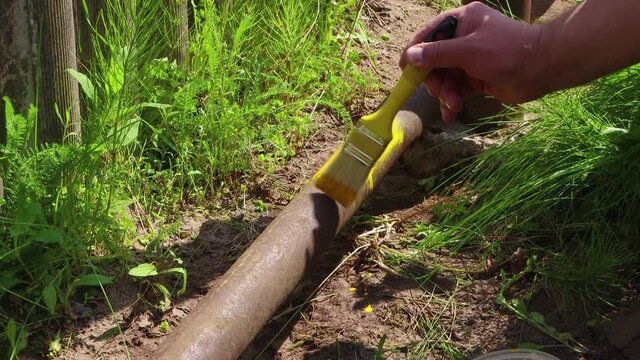 A man's hand paints a pipe with a brush with yellow paint. The concept of preventing rust and protecting the metal surface. Work on the maintenance and repair of the pipeline. UHD 4K.
