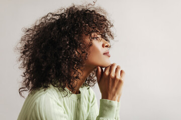 Profile portrait of curly brunette woman in green top looking straightforward. Dark-skinned lady poses on white background. © Look!