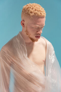 Studio portrait of shirtless albino man wrapped in plastic sheet