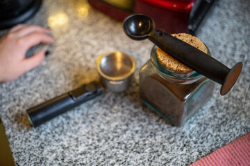 Closeup shot of a glass jar with ground coffee, spoon and portafilter on granite texture