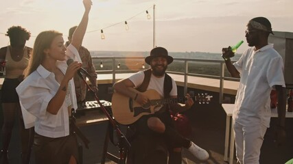 Slowmo of musicians performing song at party on rooftop terrace on nice summer evening