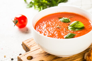 Tomato soup with basil at white table. Summer cold vegan dish.