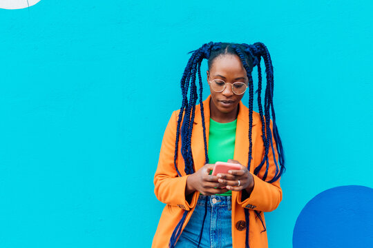 Italy, Milan, Woman with braids using smart phone against blue wall