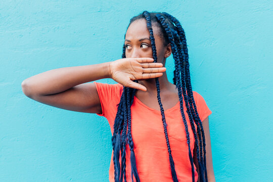 Italy, Milan, Young woman covering mouth in front of blue wall