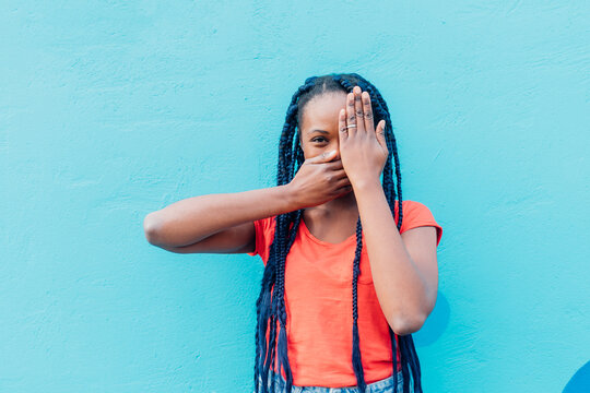 Italy, Milan, Young woman covering mouth and eye in front of blue wall