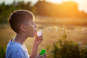 Child blowing soap bubbles on a summer day at sunset nature.