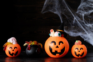 Halloween jack o lanterns pumpkins with sweets on black wooden background with spider web