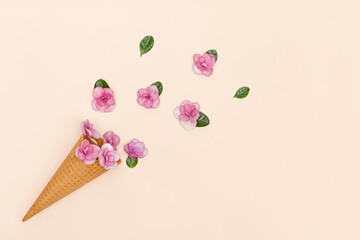 Waffle ice cream cone with pink small flowers and green leaves around Minimal summer concept
