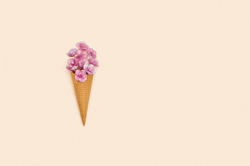 Waffle ice cream cone with pink small flowers on millennial pink colored background with copy space.