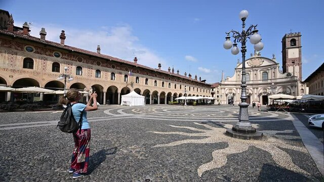 Vigevano, Lombardy, Italy. July 2021. Footage of a middle-aged tourist is photographing the facade of the cathedral of San Ambrogio. Beautiful summer day.