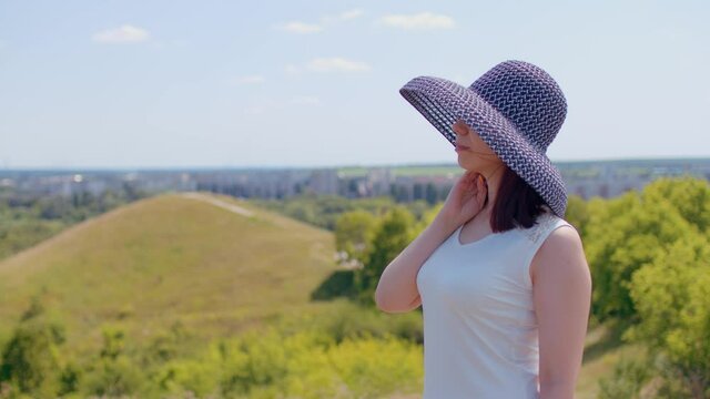 A beautiful woman in a white dress and an elegant hat poses against the background of nature. Beautiful elegant lady walking in the park wearing a hat and summer dress. Romantic image of a female