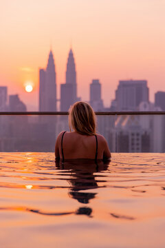 Travel lifestyle view of girl watching golden sunrise at infinity pool over skyscrapers and city horizon in Kuala Lumpur, Malaysia.