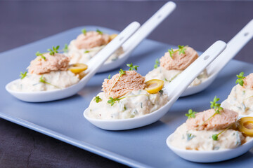 Cold appetizer made from cod liver, cod caviar, olives, cucumber and microgreens on serving spoons. Traditional cold dish. Close-up, blue plate, black background.