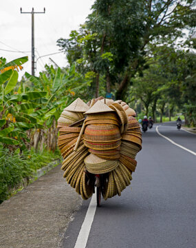 Travel lifestyle view of locals selling a lot of hats on bicycle in Ubud, Bali, Indonesia.