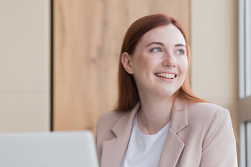 Close-up photo of a red haired business woman smiling while sitting at a computer, got a satisfactory result
