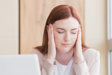 Close-up photo of a red haired business woman with a severe toothache and a headache at the computer, overwork, stress and depression