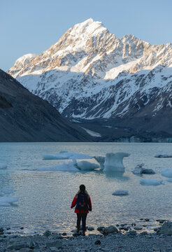 Travel lifestyle view of person hiking at frozen alpine Hooker Lake, with icebergs under Mount Cook mountain, during winter in Mount Cook National Park, on the south island of New Zealand.