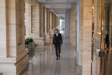 Office worker in black suit walking on the street near modern office building. 
