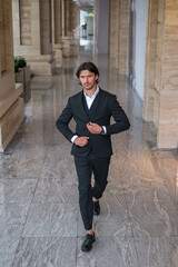 Young successful business man in black suit walking on the street near modern office building. 