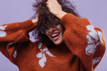 Close-up portrait of excited curly woman ruffles hair. Joyful lady in red sweater smiles sincerely...