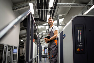 Portrait of smiling printer standing by printing machine in print house.