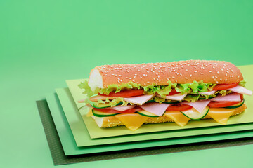 Beautiful juicy grilled baguette sandwich with ham and vegetables on green background. Space for text. High quality photo