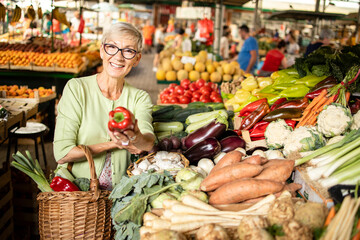Portrait of senior caucasian woman buying fresh organic vegetables and fruit at market place and holding bag full of healthy food.