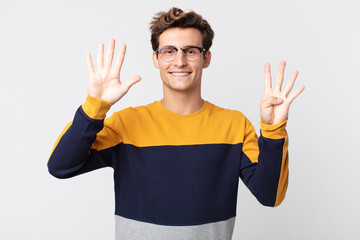 young handsome man smiling and looking friendly, showing number nine or ninth with hand forward,...