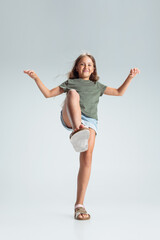 Naklejka premium Full-length portrait of beautiful preschool smiling girl stepping in air isolated on gray studio background. Childhood, education, emotion concept