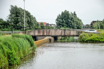 Fototapeta na wymiar Lansingerland, The Netherlands, July 27, 2021: low concrete bridge for cars passing a canal and a bicycle path between the polder and the town of Berkel