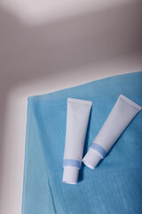 Two white mockup tubes, no label on blue fabric, with natural solid shadows. Template, copy space. Face skin care cosmetics, creme