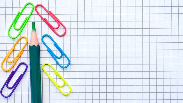 Multicolored  paper clips and Green pencil on the blank checkered page.