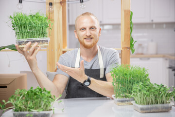 Happy farmer man sell microgreen sprouts baby beans pea and sunflower on home background