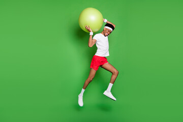 Profile photo of sportive guy jump hold big fitball wear t-shirt shorts sneakers isolated green color background