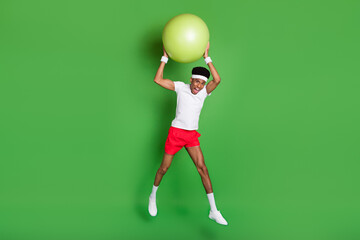 Full length photo of shocked funny dark skin guy dressed sport outfit throwing fit ball jumping isolated green color background