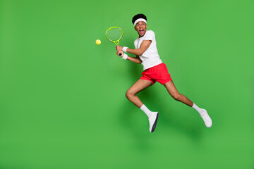 Fototapeta na wymiar Full length photo of cute funky dark skin man wear white t-shirt jumping high playing squash isolated green color background