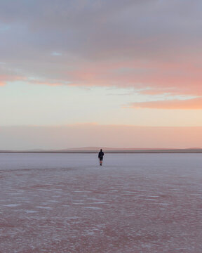 Travel lifestyle view of person walking on dry pink salt lake Bumbunga Lake at sunset, near Adelaide, South Australia.
