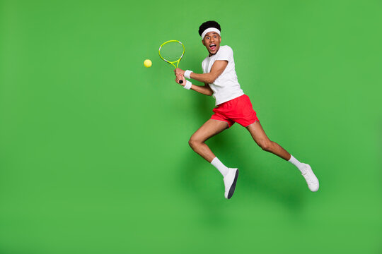Full length photo of cute funky dark skin man wear white t-shirt jumping high playing squash isolated green color background