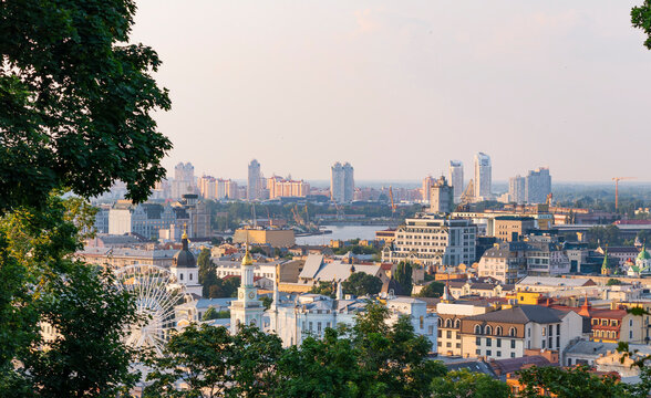 A panoramic view of the Podil,the old central part of Kiev,a top view of the roofs of houses,domes of churches,a bell tower with a clock,a Ferris wheel. Silhouettes of new modern buildings are visible