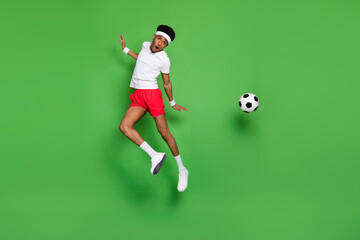 Fototapeta na wymiar Photo of team player guy jump carefree kick soccer ball wear white t-shirt shorts sneakers isolated green color background