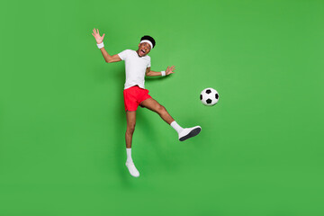 Fototapeta na wymiar Full length photo of strong excited dark skin guy dressed sport outfit jumping playing football isolated green color background
